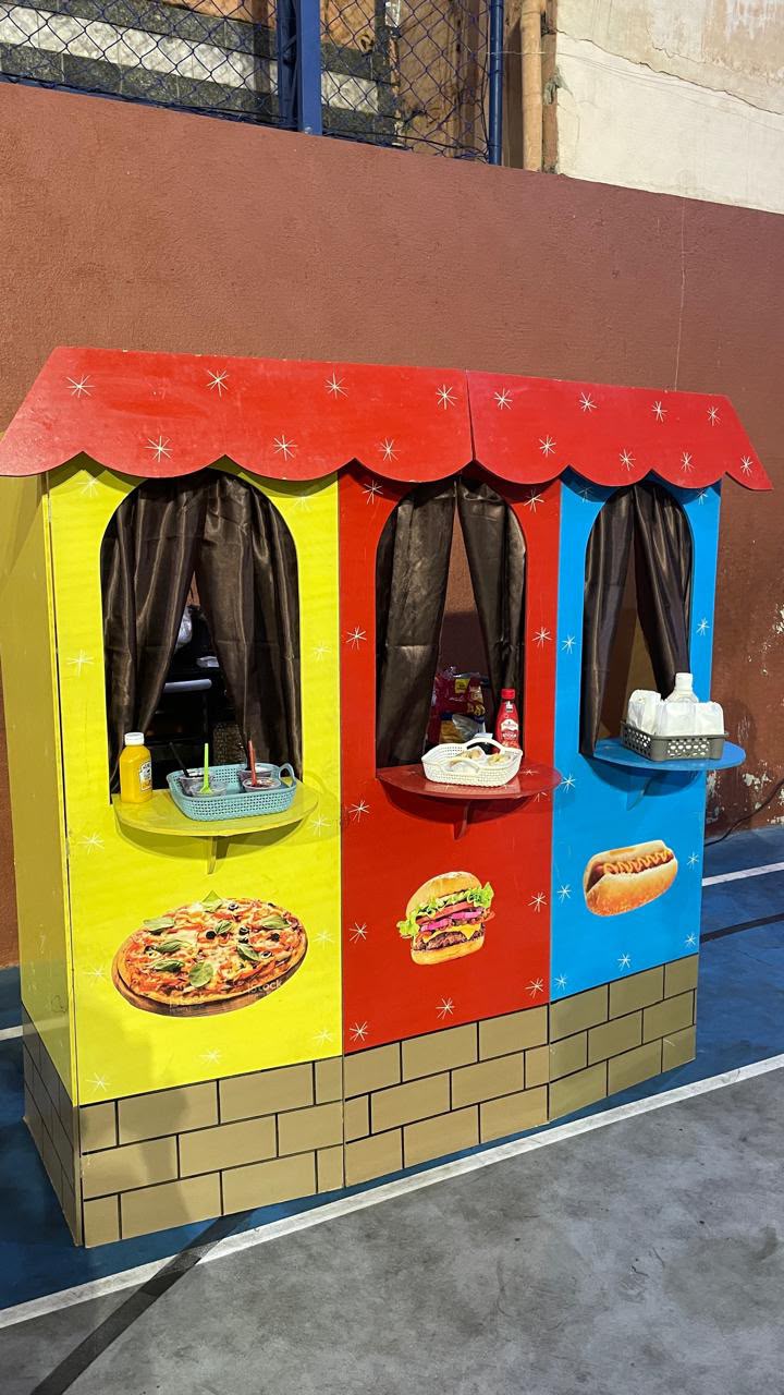 Barraquinhas coloridas da Fest Family com estações de pizza, hambúrguer e hot dog montadas para evento
